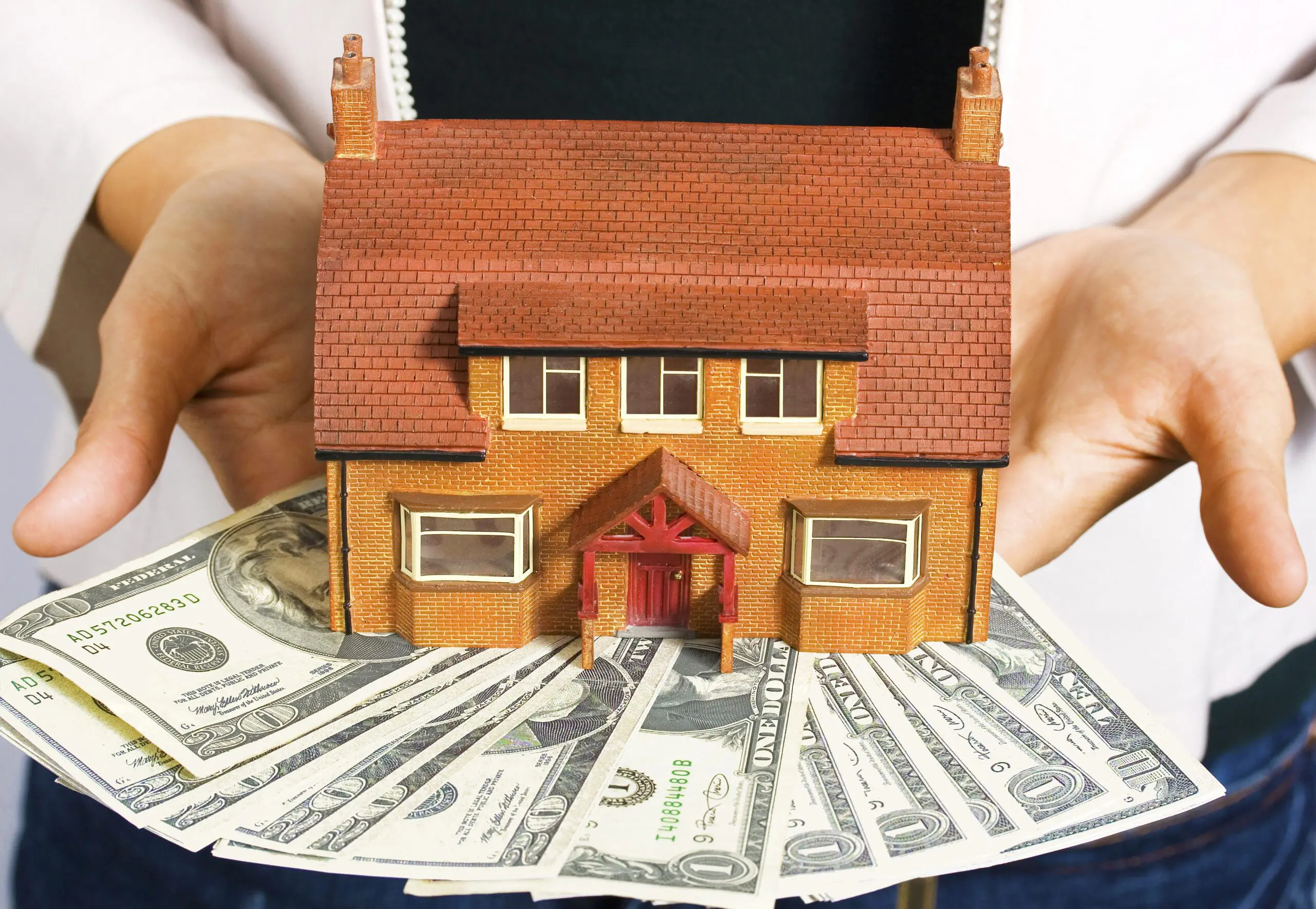 a person holding a miniature house and some dollar bills SBI 300186756 scaled